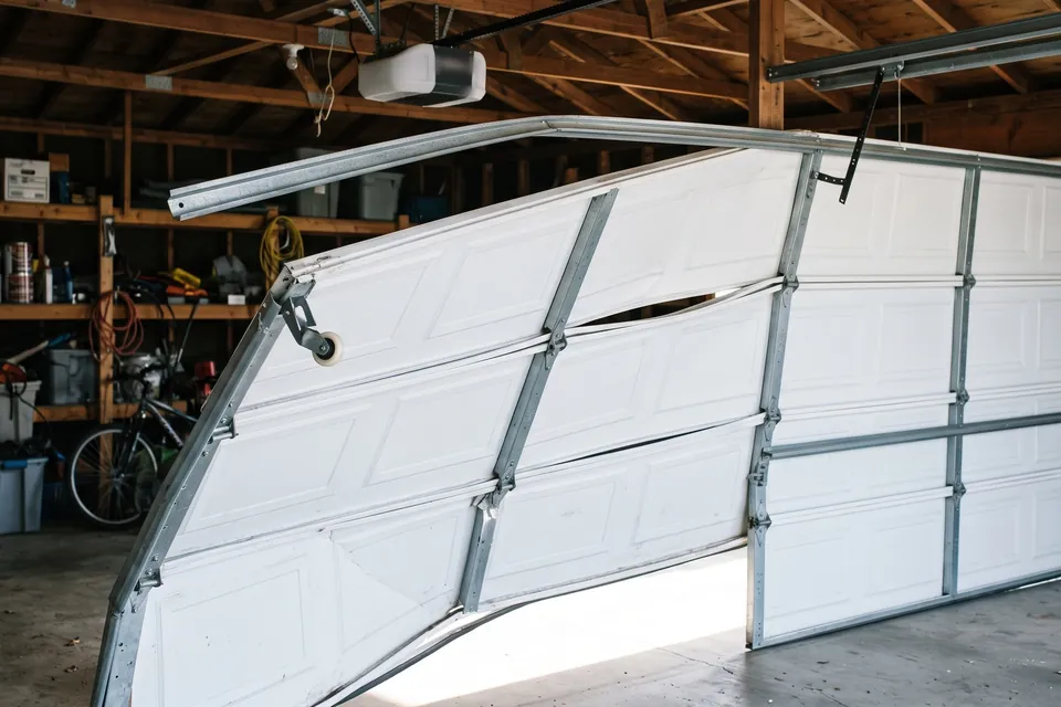 A garage door hanging out of its track at one corner with the roller clear of the rail
